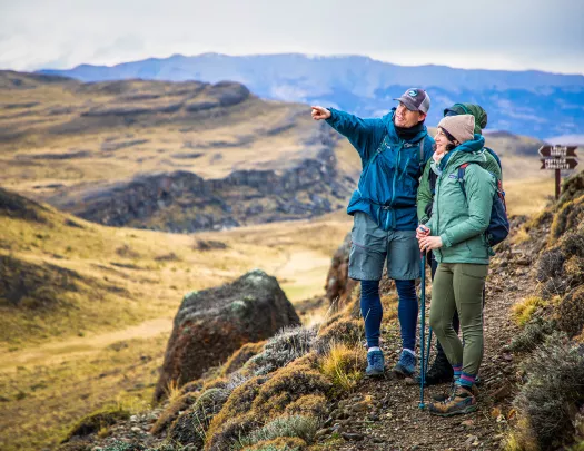 Three guests on hillside trail, one pointing towards something off-frame. 