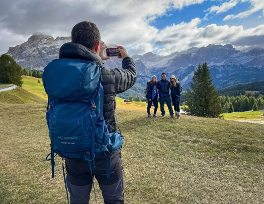 One guest taking photo of other three, mountains behind them.
