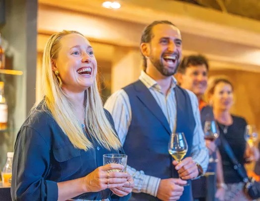 Group of men and women smiling while holding glasses of wine and spirits
