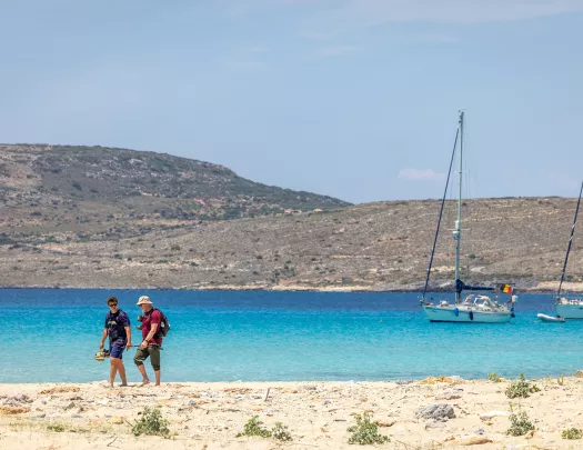Two people on the beach walking next to the ocean with their shoes in hand