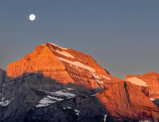 Orange sunset painted onto mountain landscape and moon peering through