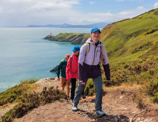 Group of people walking on a dirt trail on a hill, with the ocean in the distance