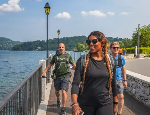 Three guests walking beside lake, road to their right.