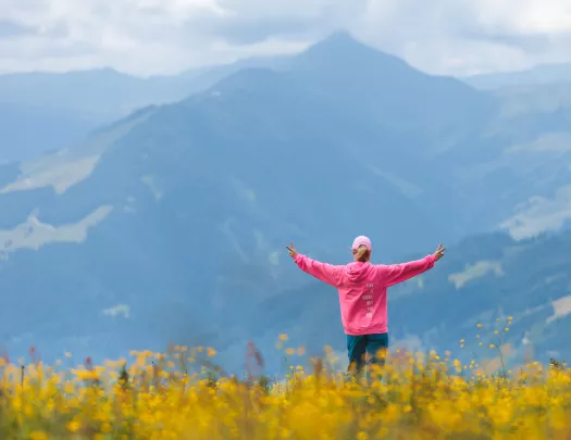 Woman wearing a pink jacket on top of a hill with her arms open
