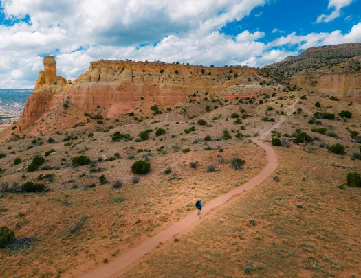 Top view of a man in blue ascending a dirt trail towards a mountain