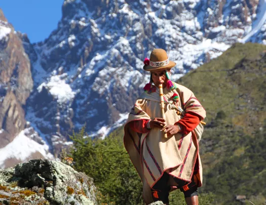 Local playing flute, craggy mountain cliffs in distance.