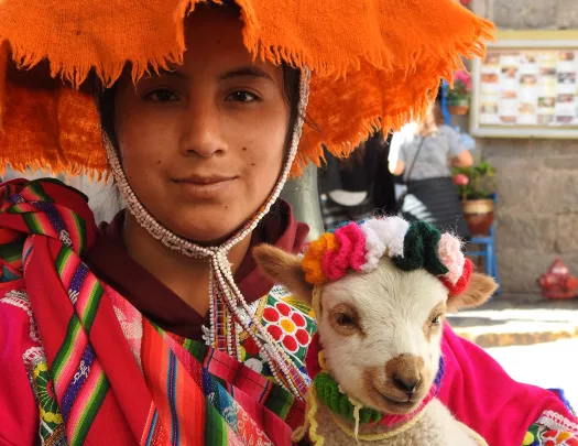 Local in colorful garb with sheep, looking at camera.