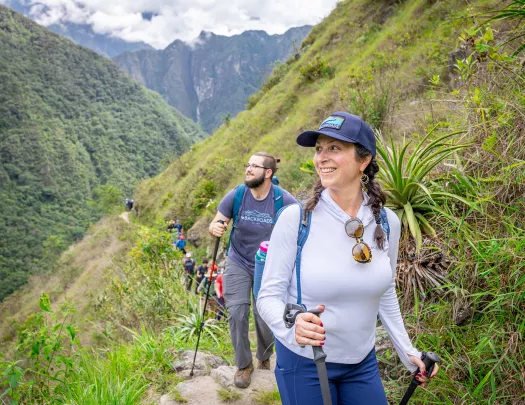 Woman and man walking on a dirt trail, smiling and looking out towards large hills