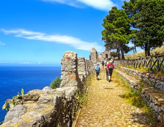 Guests walking next to ocean cliffside, towards small sandstone building.