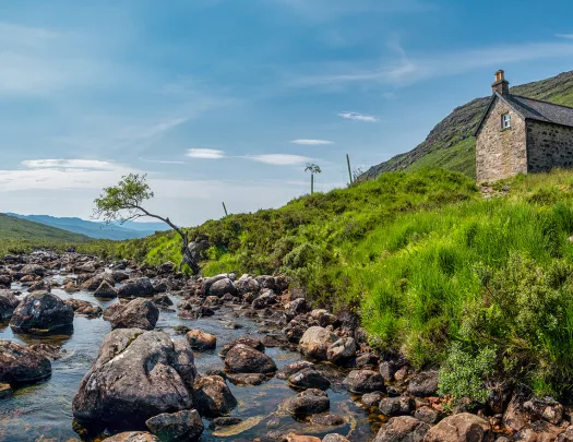 Boulders scattered through a river with a house on top of a small hill