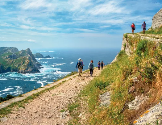 Group of guests walking on cliffs edge, large craggy island, ocean to their left.