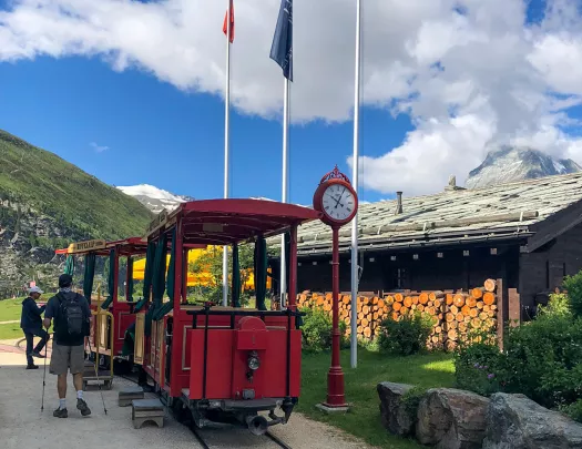 Guests at small red trolley, flags, building around them.
