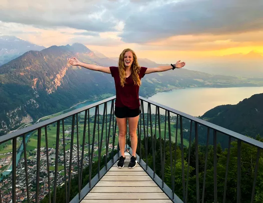 Young guest above mountain town, cliffs, lake, clouds in distance. 